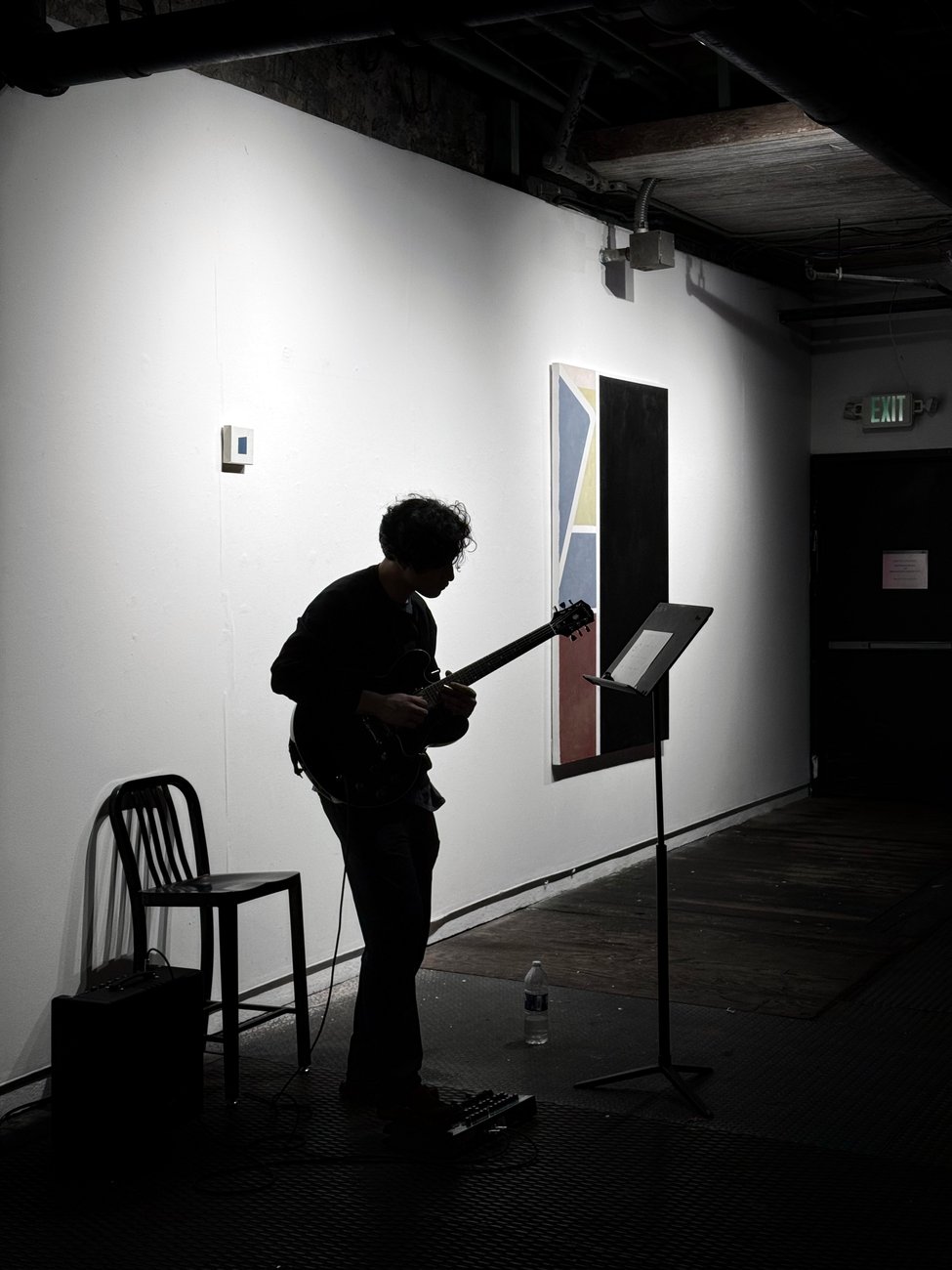 Warren performing guitar, silhouetted against a gallery wall